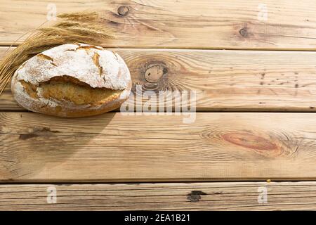 Vista dall'alto di una pagnotta di pane appena sfornata con crosta crosta e decorazione di orecchie di grano maturo. Segale e farina di grano. Foto Stock