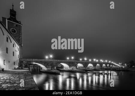Vista sul ponte in pietra di Ratisbona di notte nella nebbia sul Danubio con la cattedrale illuminata e la storica città vecchia, la Germania Foto Stock