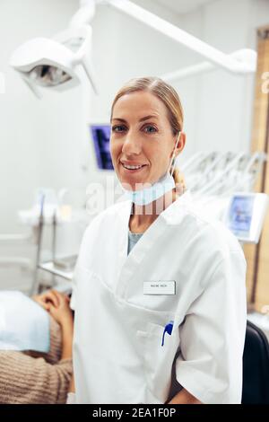 Ritratto di esperto dentale fiducioso nella sua clinica. Dentista femminile che indossa camice da laboratorio guardando la fotocamera e sorridendo. Foto Stock