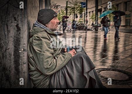 L'uomo senza tetto siede su un muro di una casa dentro la pioggia Foto Stock