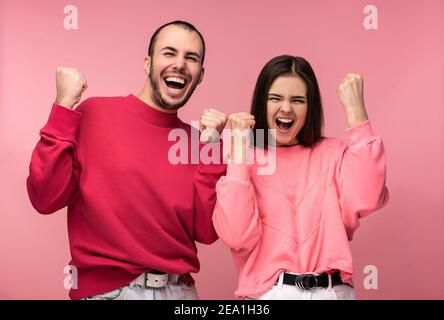 Foto di attraente uomo con barba in abiti rossi e donna in rosa sorriso e rallegrarsi qualcosa. Coppia sembra divertente, isolato su sfondo rosa Foto Stock