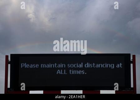 Uno schermo richiede che il distanziamento sociale debba essere mantenuto a. tutti i tempi sotto un doppio arcobaleno Foto Stock