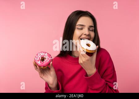 Foto di attraente signora tiene caramelle di ciambelle di cibo dolce usura casual felpa rosa isolato colore rosa sfondo Foto Stock