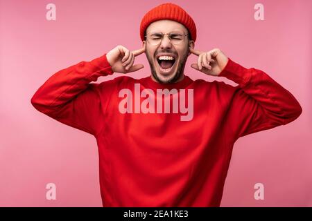 Foto di un uomo attraente con barba in occhiali e abiti rossi. Rasature e tappi per orecchie maschili, isolati su sfondo rosa Foto Stock