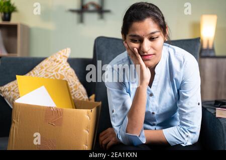 Preoccupata giovane donna d'affari seduta tristemente sul divano a casa a causa della perdita di lavoro, di lavoro o licenziato dal lavoro Foto Stock