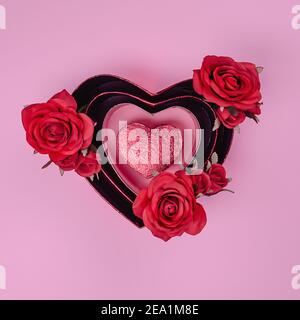 Amore o concetto di giorno di San Valentino. Rosse bellissime rose in scatola regalo a forma di cuore con cuore rosso su sfondo rosa. Vista dall'alto. Foto Stock