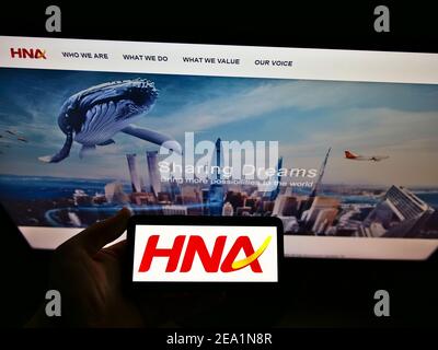 Persona che detiene smartphone con il logo della società cinese conglomerato HNA Group Co. Ltd. Sullo schermo di fronte al sito web. Mettere a fuoco il display del telefono. Foto Stock