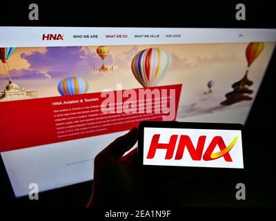 Persona che detiene il telefono cellulare con il logo della società cinese conglomerato HNA Group Co. Ltd. Sullo schermo davanti alla pagina web. Concentrarsi sul display dello smartphone. Foto Stock