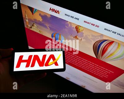 Vista ad alto angolo della persona che tiene il telefono cellulare con il logo del conglomerato cinese HNA Group sullo schermo davanti alla pagina web. Mettere a fuoco il display del telefono. Foto Stock