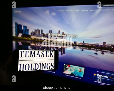 Persona che detiene smartphone con il logo della società di investimento Singaporean Temasek Holdings sullo schermo di fronte al sito web. Mettere a fuoco il display del telefono. Foto Stock