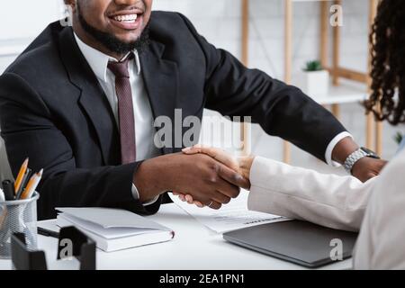 Irriconoscibile responsabile di assunzione afroamericano scuotendo la mano di candidato vacante durante il colloquio di lavoro in ufficio Foto Stock