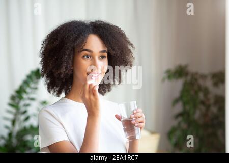 Felice sorridente giovane afroamericana che prende pillola o vitamina con olio di fegato di merluzzo omega-3 Foto Stock