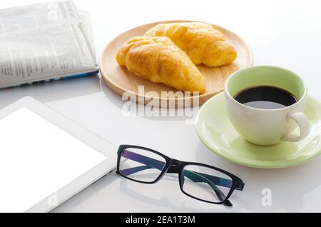 Bicchieri alla scrivania con smartphone, croissant, quotidiano e caffè cup.in al mattino Foto Stock