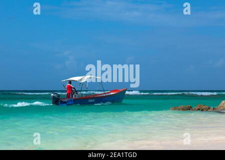 Uomini barbadiani in gonna rossa sulla barca blu in acque azzurre del mare dei Caraibi. Worthing spiaggia a Barbados. Foto Stock