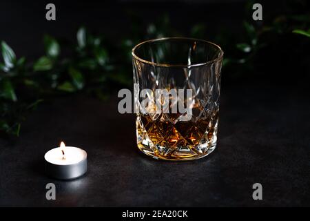 Primo piano di un vetro antico riempito con whisky o bourbon. Il tumbler si erge su uno sfondo di pietra, che crea una scena rustica (fotografia alimentare) Foto Stock