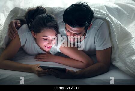 Primo piano giovane dolce coppia sul letto guardando qualcosa sul Tablet Gadget, rilassarsi in camera da letto. Foto Stock