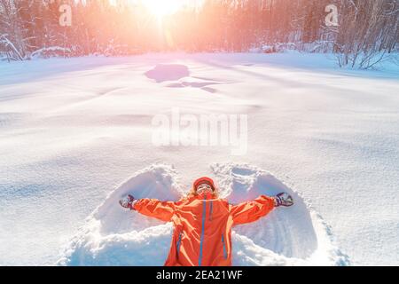 Happy Girl fa l'impronta di angelo nella neve. Divertimento invernale e temperamento e concetto di salute Foto Stock