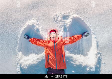 Happy Girl fa l'impronta di angelo nella neve. Divertimento invernale e temperamento e concetto di salute Foto Stock