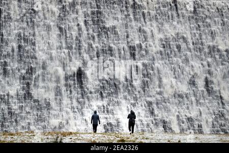 La gente guarda come l'acqua scende lungo la diga di Derwent nel Peak District, con la neve pesante impostata per portare disturbo al sud-est dell'Inghilterra e dell'Anglia orientale, mentre i venti amaramente freddi affondano gran parte della nazione. Data immagine: Domenica 7 febbraio 2021. Foto Stock