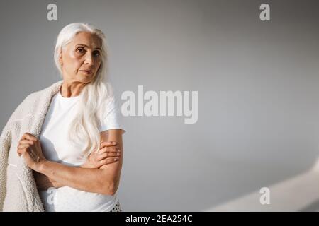 Bella donna anziana dai capelli bianchi in posa con le braccia incrociate isolato sopra sfondo grigio Foto Stock