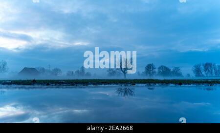 Tramonto con capanna, specchio d'albero, valle del Reno. Nuvole colorate e neve sul campo. Farbade Wolken beim Sonnenuntergang im Rheintal, Baum Spiegelung Foto Stock