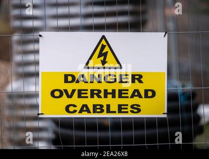 Pericolo cavi sospesi segnale pulito moderno in cantiere con bullone di alleggerimento triangolare per scosse elettriche giallo e rulli elettrici cavo Foto Stock