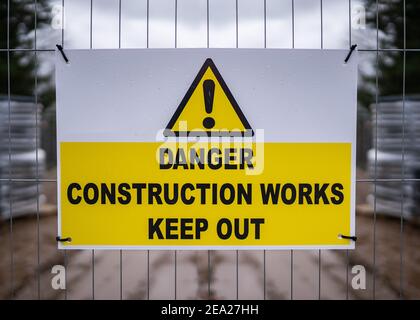 Pericolo cantiere tenere fuori moderno pulito segno giallo con punto esclamativo triangolare attaccato alla recinzione metallica intorno all'edificio opere Foto Stock