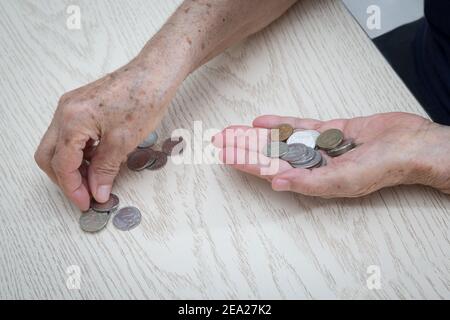 Mani di una vecchia donna in pensione primo piano sullo sfondo di un tavolo leggero che conta una trifla, monete di ferro di denaro russo. Il concetto del piccolo siz Foto Stock