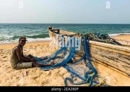 Uomo che fissa le reti nelle sue barche da pesca su una spiaggia a Robertsport, Liberia Foto Stock