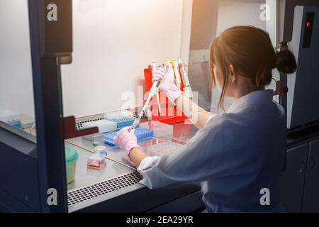 Donna ricercatrice scienziato lavora con pipette elettroniche e reagenti chimici per fare l'analisi genetica medica o vaccino covid-19 Foto Stock