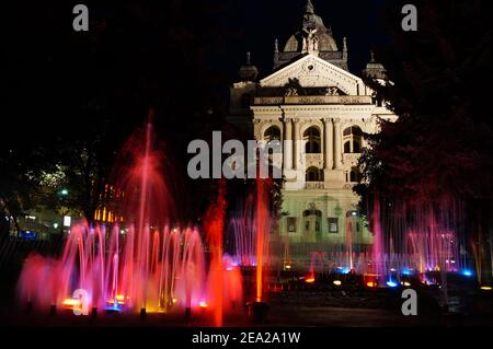 Vista notturna presso la colorata fontana cantata nella città di Kosice in Slovacchia con il teatro di Stato sullo sfondo Foto Stock