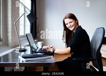 Una giovane donna lavora alla sua scrivania in un ambiente di ufficio. Foto Stock