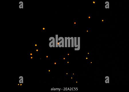 Bokeh arancione su sfondo nero, scintille brucianti e sfocate dal fuoco. Particelle di braci brucianti volano e brillano isolate nel cielo notturno 2021. Foto Stock