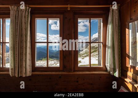 Vista attraverso una finestra nella camera del rifugio Schlüter sulla soleggiata Valle Villnöss e sulle Alpi Sarntal in autunno, Dolomiti, Alto Adige, Italia Foto Stock