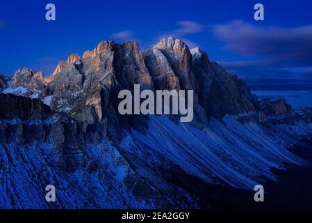 Le pareti rocciose innevate e le scogliere delle vette Geisler dei monti Puez-Odle con branchi di nuvole illuminano all'alba, Dolomiti, Alto Adige, Italia Foto Stock