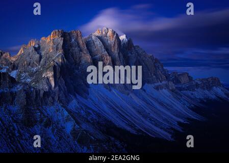 Le pareti rocciose innevate e le scogliere delle vette Geisler dei monti Puez-Odle con branchi di nuvole illuminano all'alba, Dolomiti, Alto Adige, Italia Foto Stock