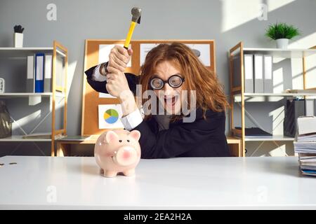 L'uomo pazzo vuole rompere la sua banca piggy con il martello e investire i suoi soldi nel business Foto Stock