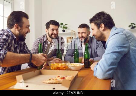 Quattro amici uomini allegri che hanno una festa a casa incontro con la birra e pizza Foto Stock