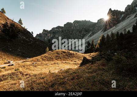 I raggi del sole del mattino tra le cime rocciose dei Puez brillano sui prati alpini di Antersasc alp in autunno, Dolomiti, Alto Adige, Italia Foto Stock