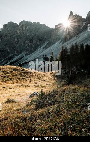 I raggi del sole del mattino tra le cime rocciose dei Puez brillano sui prati alpini di Antersasc alp in autunno, Dolomiti, Alto Adige, Italia Foto Stock