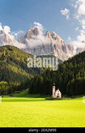 Paesaggio autunnale delle Dolomiti con la Cappella Ranui a Villnöss di fronte alle foreste e rocce delle vette Puez-Odle sotto il sole, Alto Adige Foto Stock