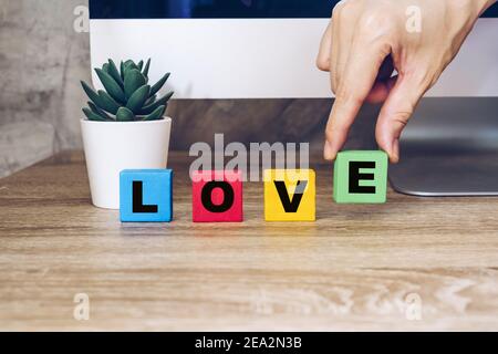 Tenere a mano il cubo di legno con il testo Love sul tavolo Foto Stock