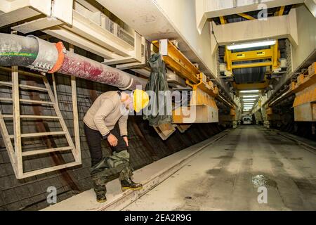 (210207) -- URUMQI, 7 febbraio 2021 (Xinhua) -- UN operaio toglie il suo impermeabile per disperdere l'umidità dal suo maglione e pantaloni nel sito di costruzione del tunnel di Tianshan Shengli nella regione autonoma di Xinjiang Uygur, 4 febbraio 2021. Il tunnel di Tianshan Shengli, con una lunghezza totale di circa 22 chilometri, è attualmente il tunnel autostradale più lungo in costruzione in Cina. Iniziato nel 2020, il tunnel, un progetto di sei anni sulla strada statale Urumqi-Yuli, passa attraverso una zona fredda e ad alta quota, con condizioni climatiche e geologiche difficili. Dopo il completamento e aperto al traffico, esso Foto Stock