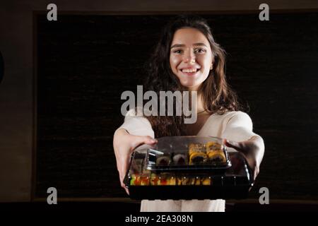 Sushi in scatola cibo sano consegna online servizio. La ragazza tiene in mano 2 set di sushi. Cucina giapponese: Panini, salsa di soia, wasabi Foto Stock