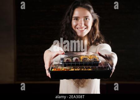 Sushi in scatola cibo sano consegna online servizio. La ragazza tiene in mano 2 set di sushi. Cucina giapponese: Panini, salsa di soia, wasabi Foto Stock