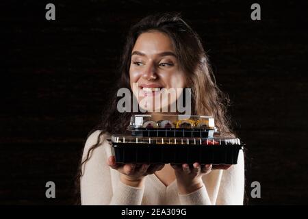 Primo piano sushi in scatola sana consegna cibo servizio online. La ragazza tiene in mano 2 set di sushi. Cucina giapponese: Panini, salsa di soia, wasabi Foto Stock