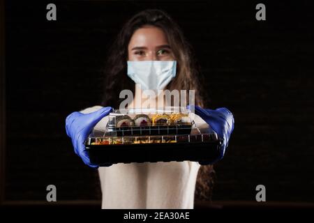 Primo piano sushi in scatola sana consegna cibo servizio online. La ragazza tiene in mano 2 set di sushi. Cucina giapponese: Panini, salsa di soia, wasabi Foto Stock