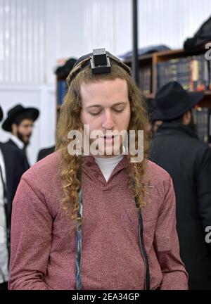 Un giovane ebreo ortodosso con lunghe preghiere di peyot al mattino servizi presso l'Ohel a Cambria Heights, Queens, New York Citytefillin, phylacteries, te Foto Stock