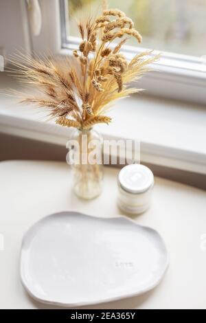 Un piatto bianco fatto di argilla fatta a mano, una candela, un vaso si trova vicino alla finestra Foto Stock