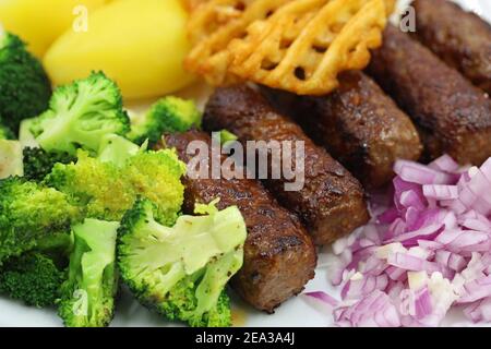 primo piano di cevapcici alla griglia con broccoli, cipolle rosse e patate, classico cibo balcanico Foto Stock